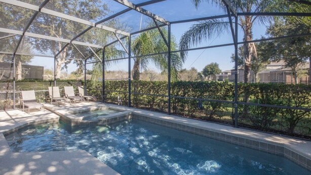 An indoor swimming pool with clear glass walls, surrounded by lounge chairs and a well-maintained garden.