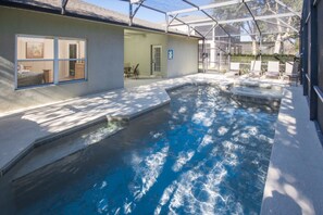 A swimming pool with a glass enclosure, a patio area with chairs, and a door leading to an interior space. - The Shire at West Haven 906 (Davenport)