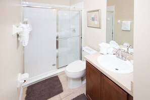 A modern bathroom with a glass shower enclosure, a white toilet, a sink with a mirror, and a wooden cabinet. - The Shire at West Haven 906 (Davenport)