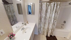 Ein Badezimmer mit weißem Waschbecken, Spiegel und Duschvorhang mit Blattmuster.
