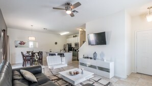 A modern living room with a black leather sofa, a white coffee table, and a dining area in the background. - Bella Vida 1300 (Kissimmee)