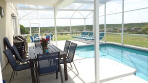 A covered outdoor area with a pool, lounge chairs, and a table with chairs. - Highlands Reserve Golf & Country Club 303 (Davenport)