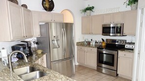 A modern kitchen with stainless steel appliances, granite countertops, and light-colored cabinetry. - Highlands Reserve Golf & Country Club 303 (Davenport)