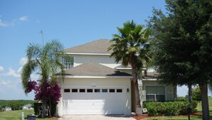 A single-story house with a white garage door, a number 303 garage sign, and a well-maintained front yard with a palm tree and flowering plants. - Highlands Reserve Golf & Country Club 303 (Davenport)