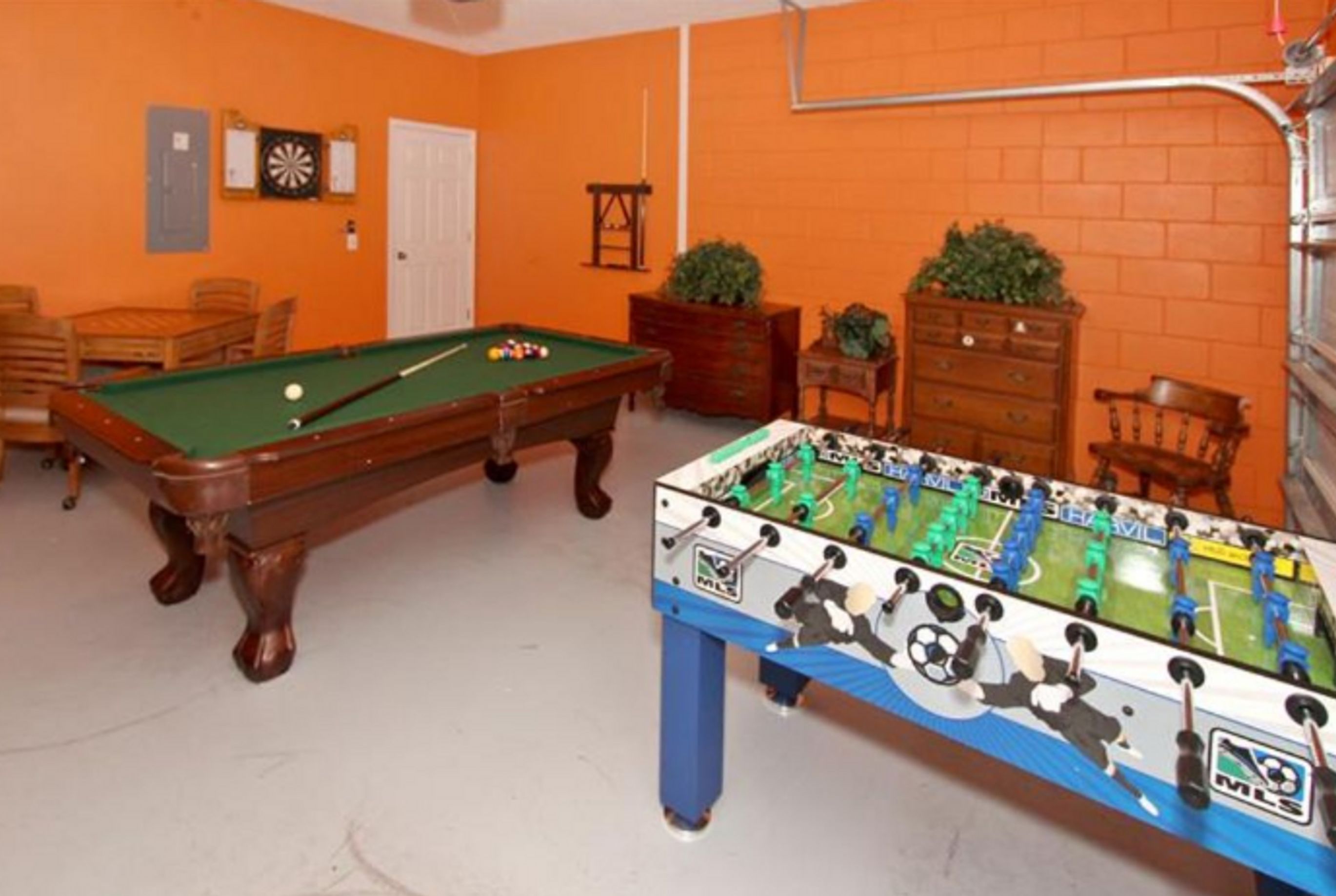 A room with two pool tables, a foosball table, and a dartboard on the wall.