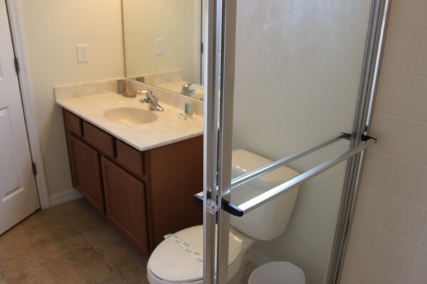 A bathroom with a white toilet, a sink with a mirror above it, and a shower area with a glass door. - Bella Vida 290 (Kissimmee)