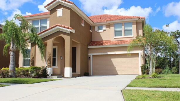 A two-story house with a red-tiled roof, beige exterior walls, and a garage.
