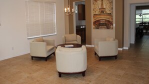 A living room with beige armchairs, a coffee table, and a painting of the Eiffel Tower.