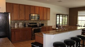 A kitchen with wooden cabinets, a granite countertop, a stainless steel refrigerator, a microwave, and a sink.