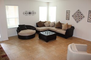 A living room with a sectional sofa, a round ottoman, and a single chair. - Bella Vida 290 (Kissimmee)