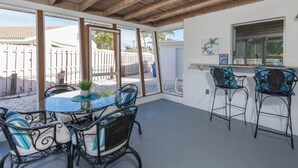 An outdoor patio with a glass table and chairs, wooden ceiling beams, and a view of a fenced area with palm trees. - Fort Myers Beach Area 540 (Fort Myers)