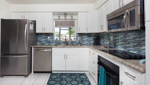 A modern kitchen with white cabinets, stainless steel appliances, a tiled backsplash, and a patterned rug. - Fort Myers Beach Area 540 (Fort Myers)