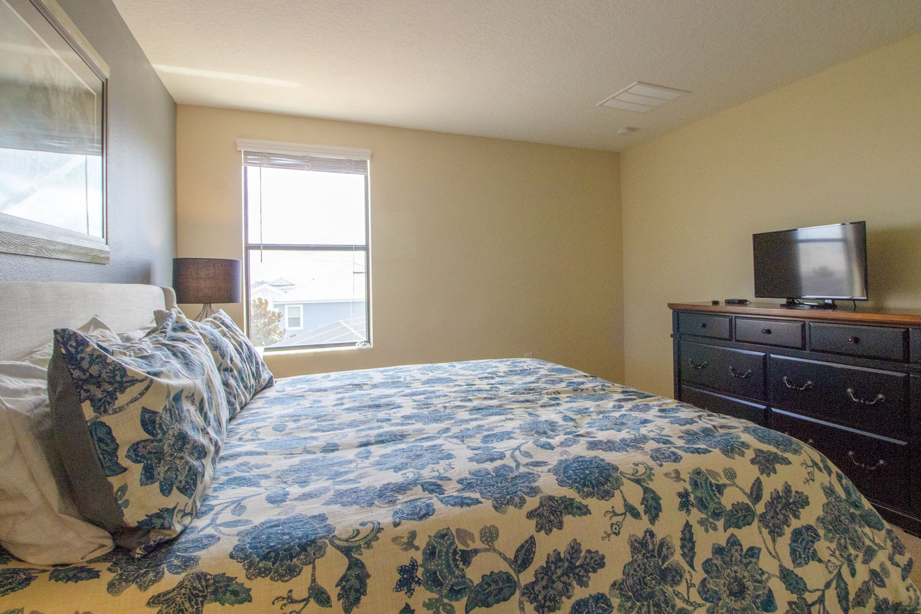 A bedroom with a bed, a dresser, a television, and a window.