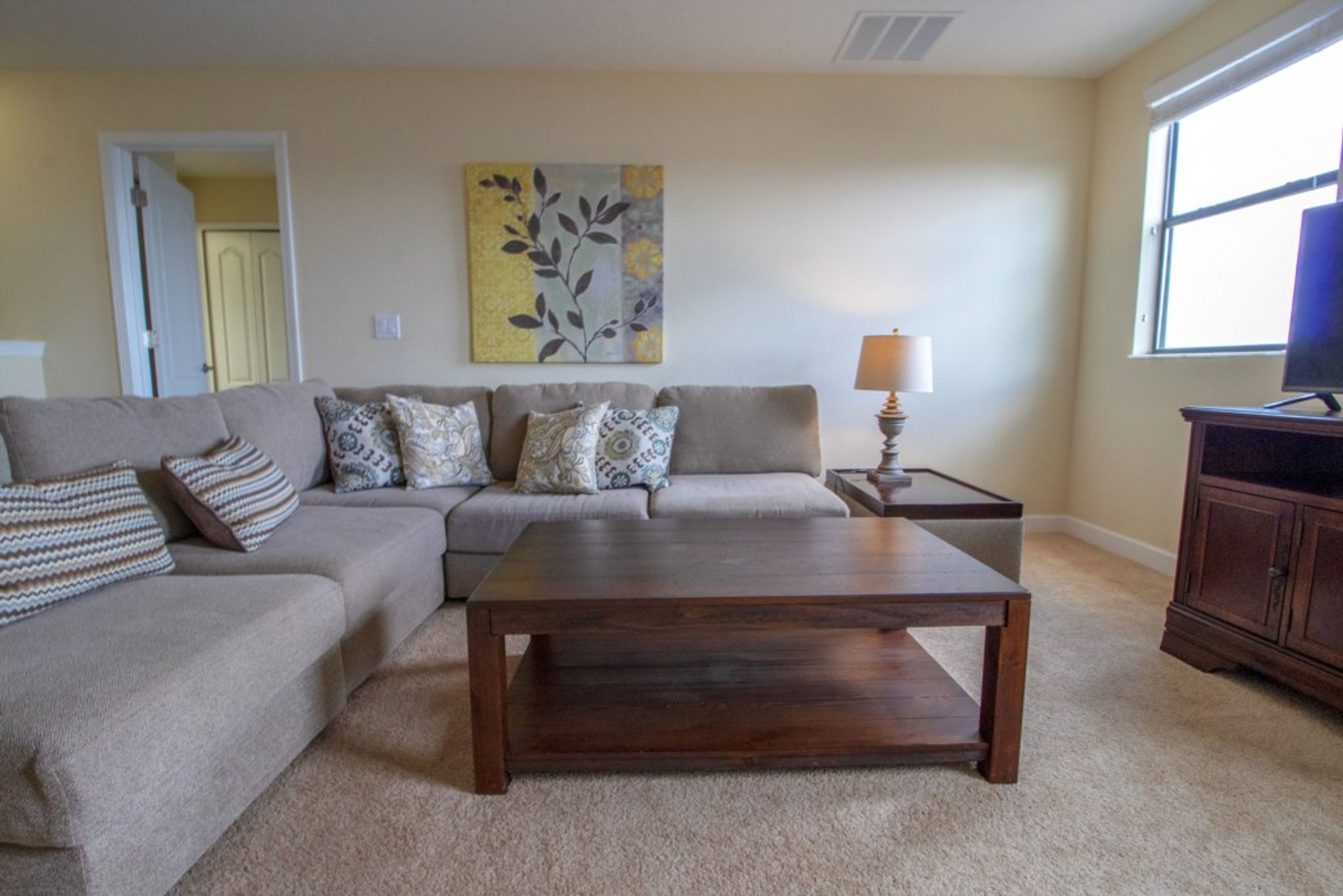 A living room with a beige sofa, a wooden coffee table, a lamp, and a television on a cabinet.
