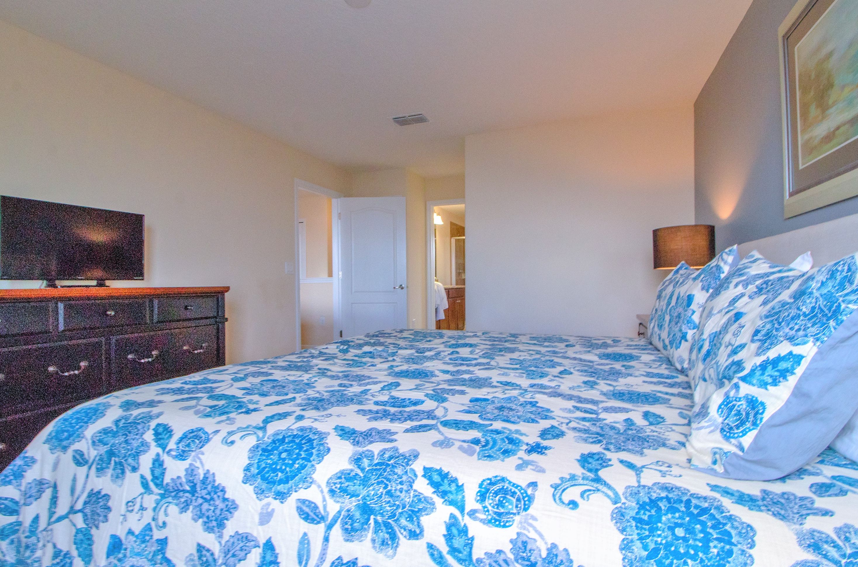 A bedroom with a bed, dresser, and a television on the wall.
