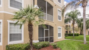 A multi-story building with balconies, a palm tree, and a well-maintained lawn. - Windsor Palms 2300 - 101 (Kissimmee)