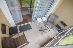 A balcony with a wicker chair, a small table, and a glass door leading to a grassy area. - Windsor Palms 2300 - 101 (Kissimmee)