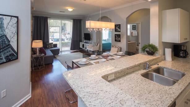 A modern kitchen with granite countertops, a double sink, and a dining area with a table set for four. - Windsor Palms 2300 - 101 (Kissimmee)