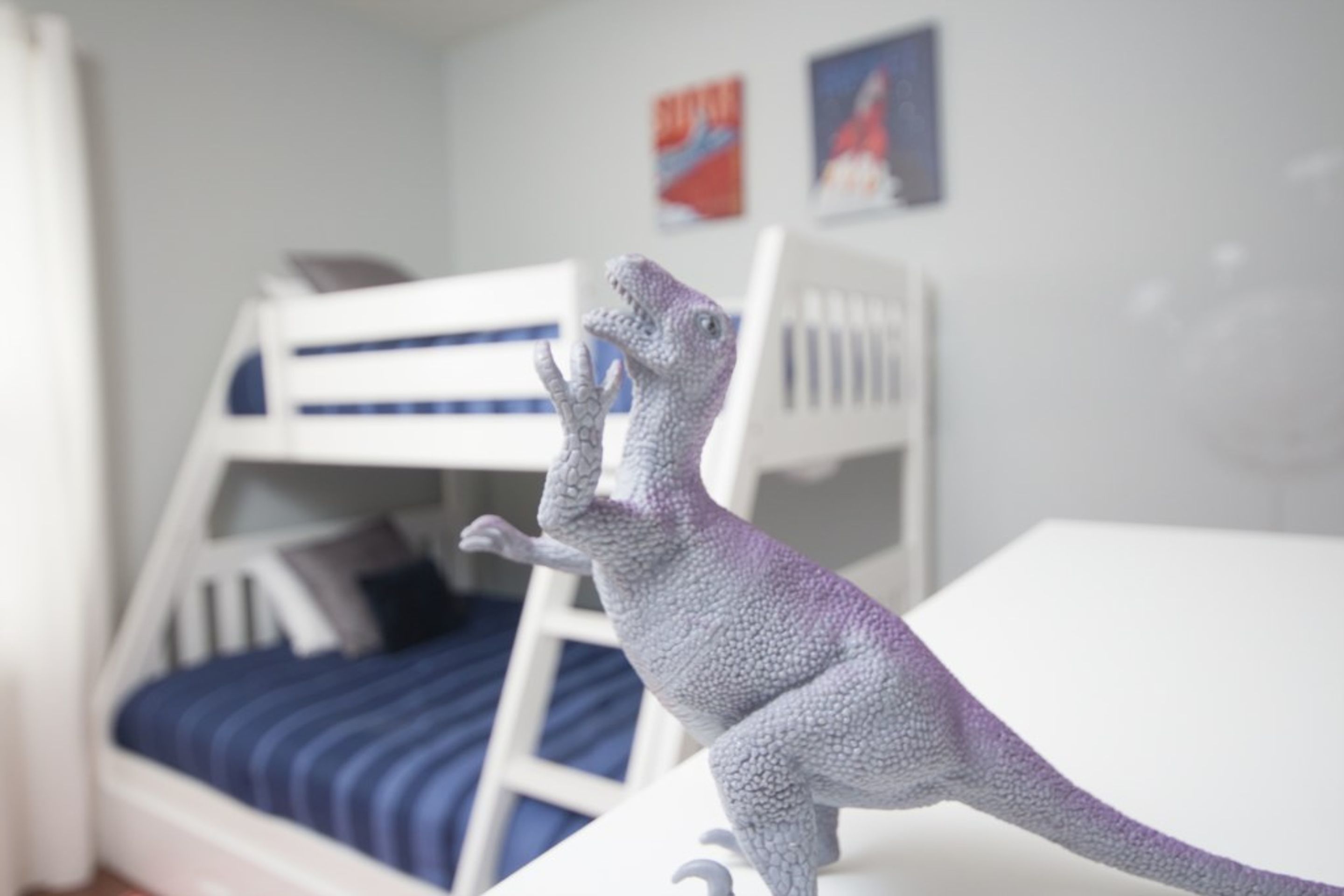 Una figura de dinosaurio sobre una superficie blanca, con literas al fondo.