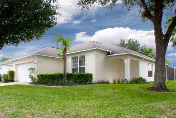 A single-story house with a front garage, a well-maintained lawn, and a large tree on the right.