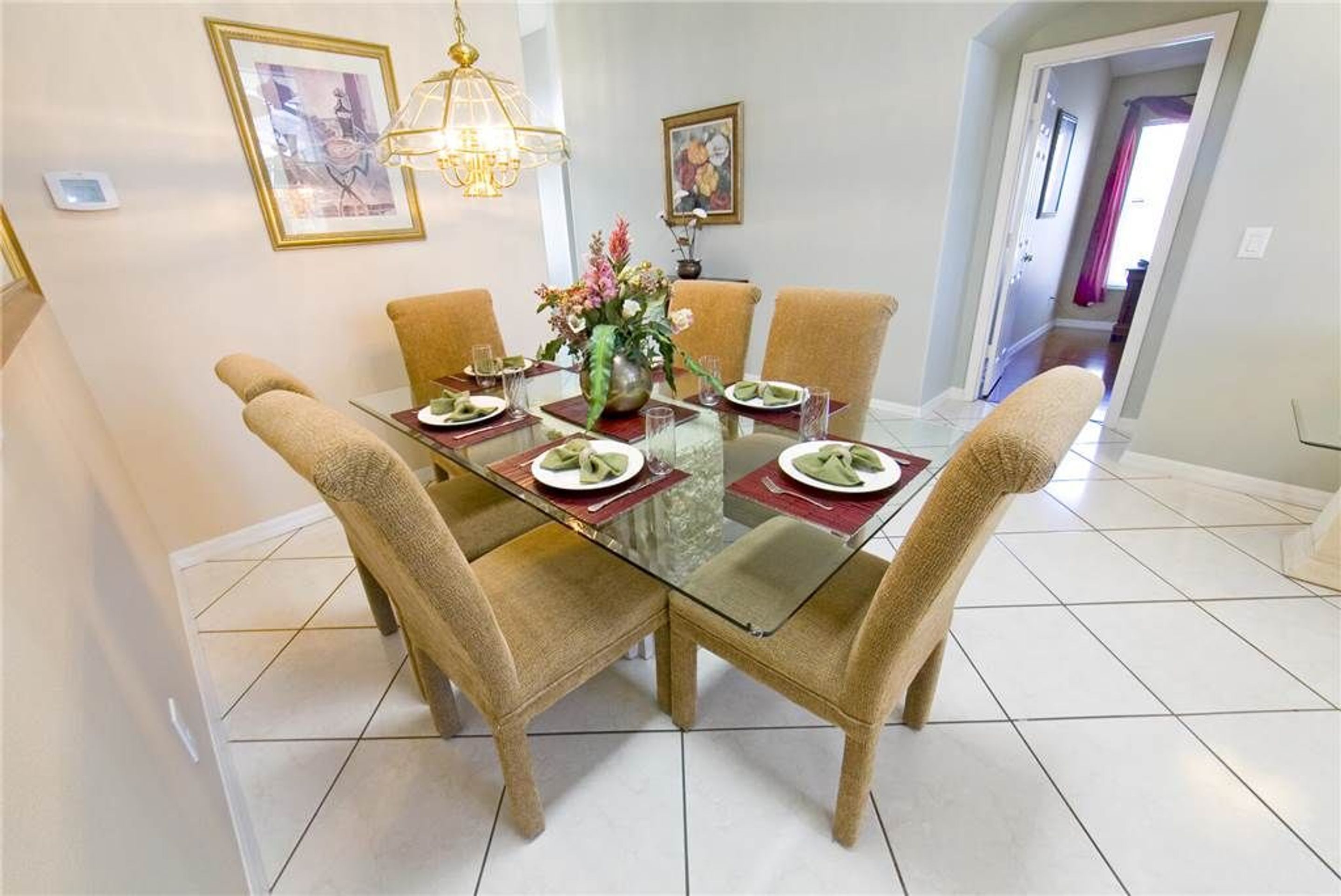 A dining area with a glass table surrounded by four chairs, a vase with flowers, and framed artwork on the walls.