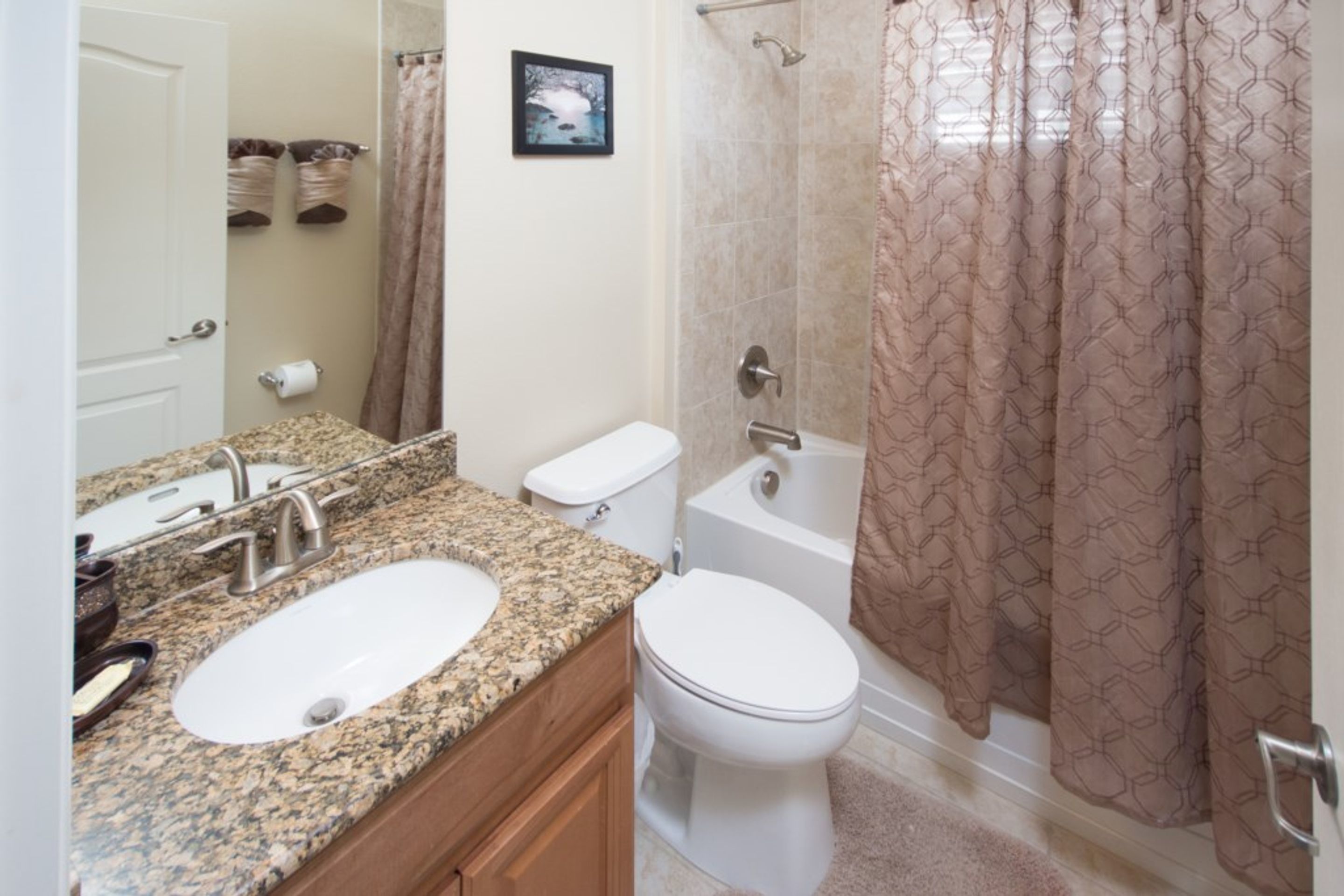 A bathroom with a granite countertop sink, a toilet, a bathtub, and a shower curtain.