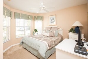A bedroom with a bed, a desk, a lamp, and a ceiling fan.