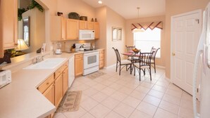 A kitchen with wooden cabinets, a microwave, an oven, a sink, and a dining area with chairs and a table. - The Hamlet at Westhaven 238 (Davenport)