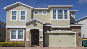 A two-story house with a garage, stone facade, and a brick driveway. - Encore Resort at Reunion 270 (Kissimmee)