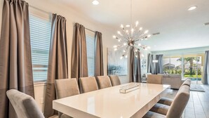 A modern dining area with a long table, cushioned chairs, and a contemporary chandelier. - Encore Resort at Reunion 270 (Kissimmee)
