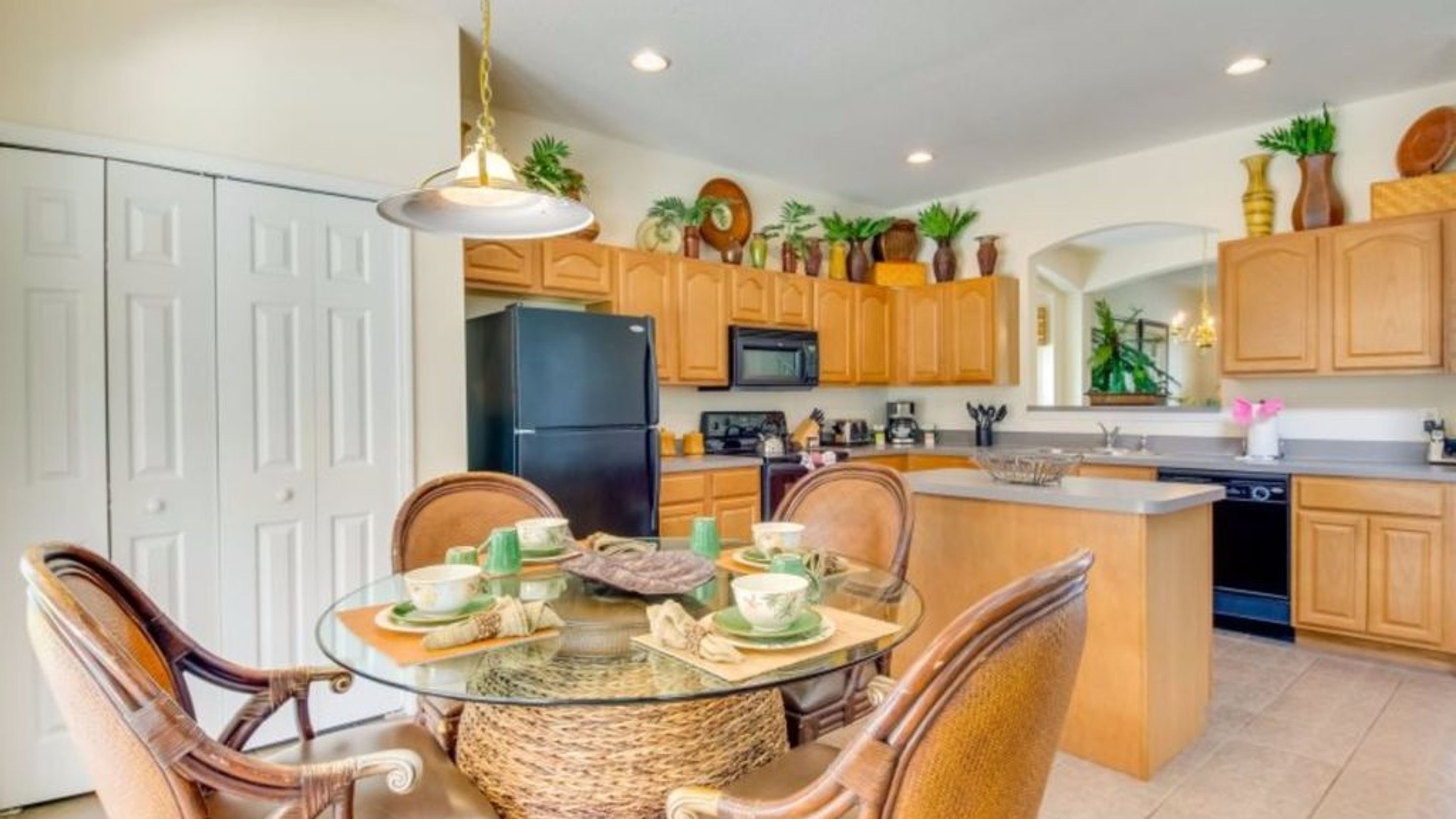 A modern kitchen with wooden cabinets, a black refrigerator, and a dining area with a glass table and wicker chairs.