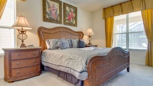 A bedroom with a wooden bed, two nightstands, a dresser, and two wall-mounted lamps. There are two framed botanical prints on the wall. - Emerald Island Resort 2801 (Kissimmee)