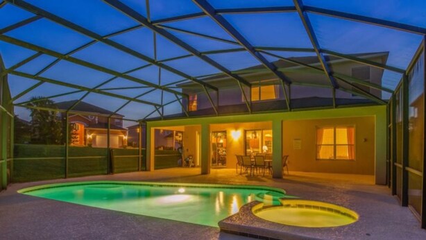 A covered outdoor swimming pool area with a house in the background. - Emerald Island Resort 2801 (Kissimmee)