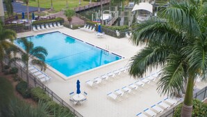 A swimming pool with lounge chairs and umbrellas, surrounded by palm trees and a view of a marina. - Fort Myers Beach Area 7327 - 409 (Fort Myers Beach)