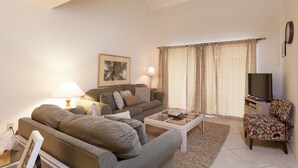 A living room with a sofa, a coffee table, a TV stand, and a patterned armchair. - Fort Myers Beach Area 7327 - 409 (Fort Myers Beach)