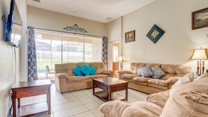 Ein Wohnzimmer mit beigefarbenen Sofas, einem Couchtisch und einem an der Wand befestigten Fernseher.