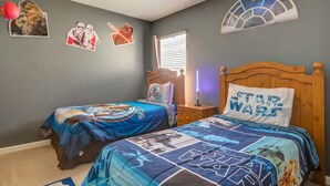 Ein Schlafzimmer mit zwei Betten, Star Wars-Betwäsche und Wanddekorationen, darunter ein Star Wars-Poster, sowie ein Fenster mit Blick auf den Himmel.