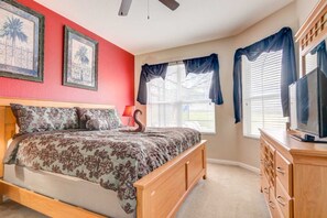 A bedroom with a bed, a dresser, a television, and two windows with curtains.
