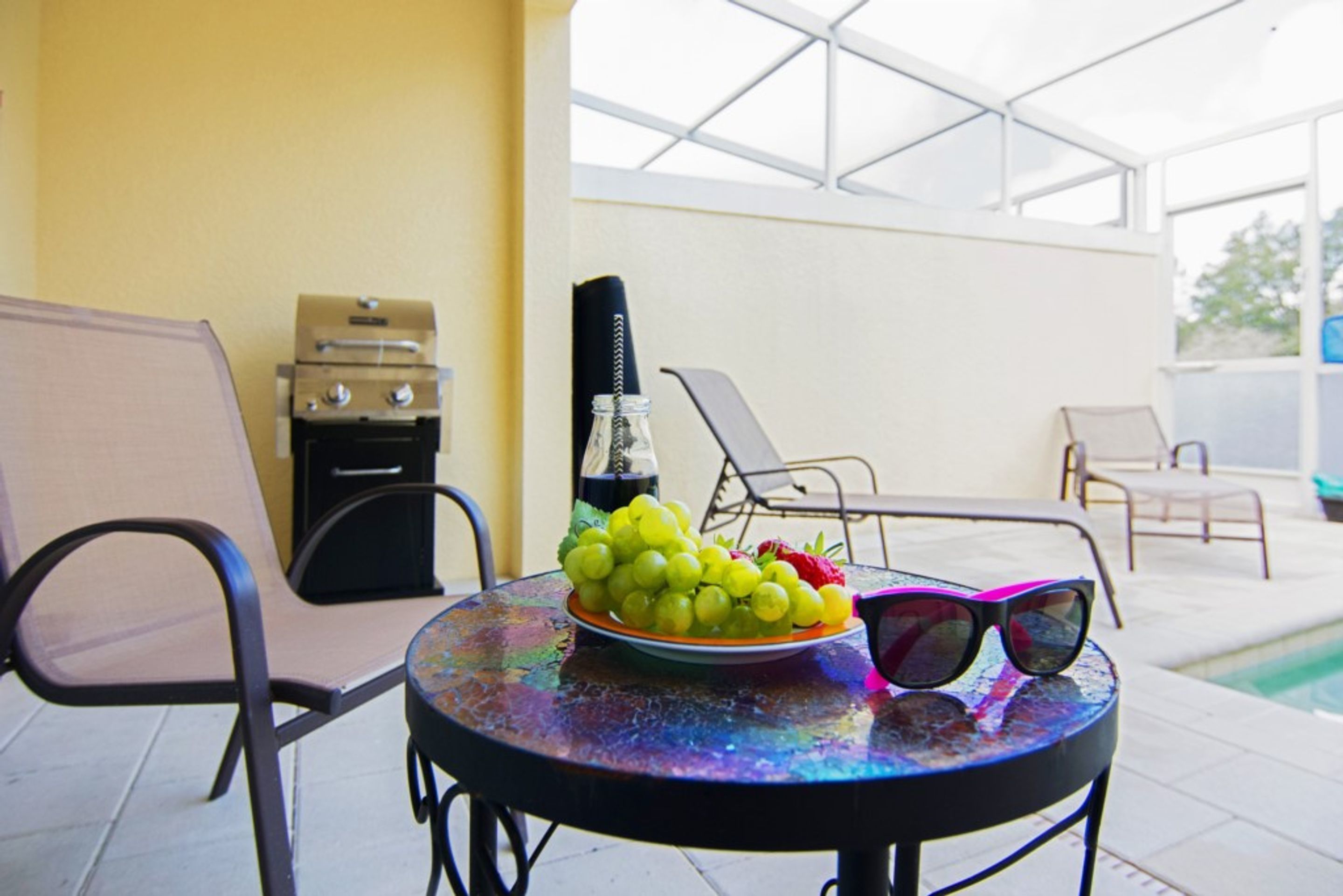 A round table with a plate of grapes and strawberries, a bottle, and sunglasses.