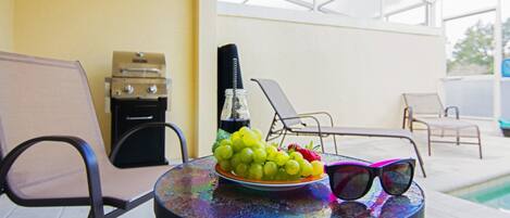 A round table with a plate of grapes and strawberries, a bottle, and sunglasses.