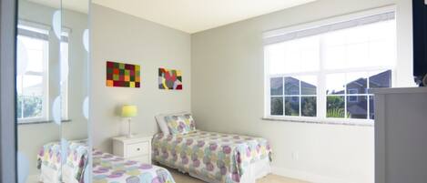 A bedroom with two beds, a window, and artwork on the wall.