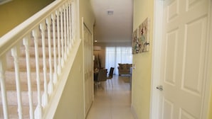 A hallway with a staircase on the left, a dining area with chairs and a table in the center, and a door on the right. - Serenity 17417 A (Clermont)