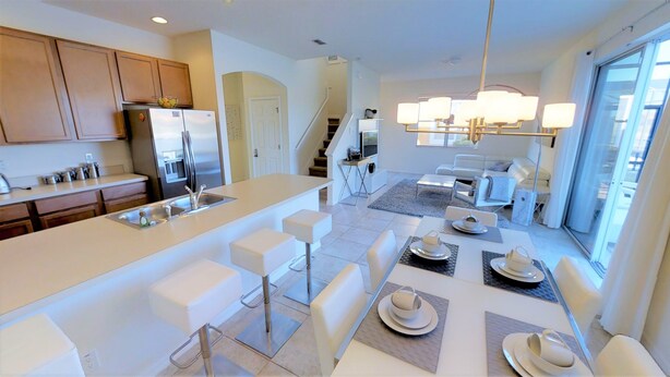 A modern kitchen with a central island, white bar stools, and a dining area with a table set for four. - Bella Vida 541 A (Kissimmee)