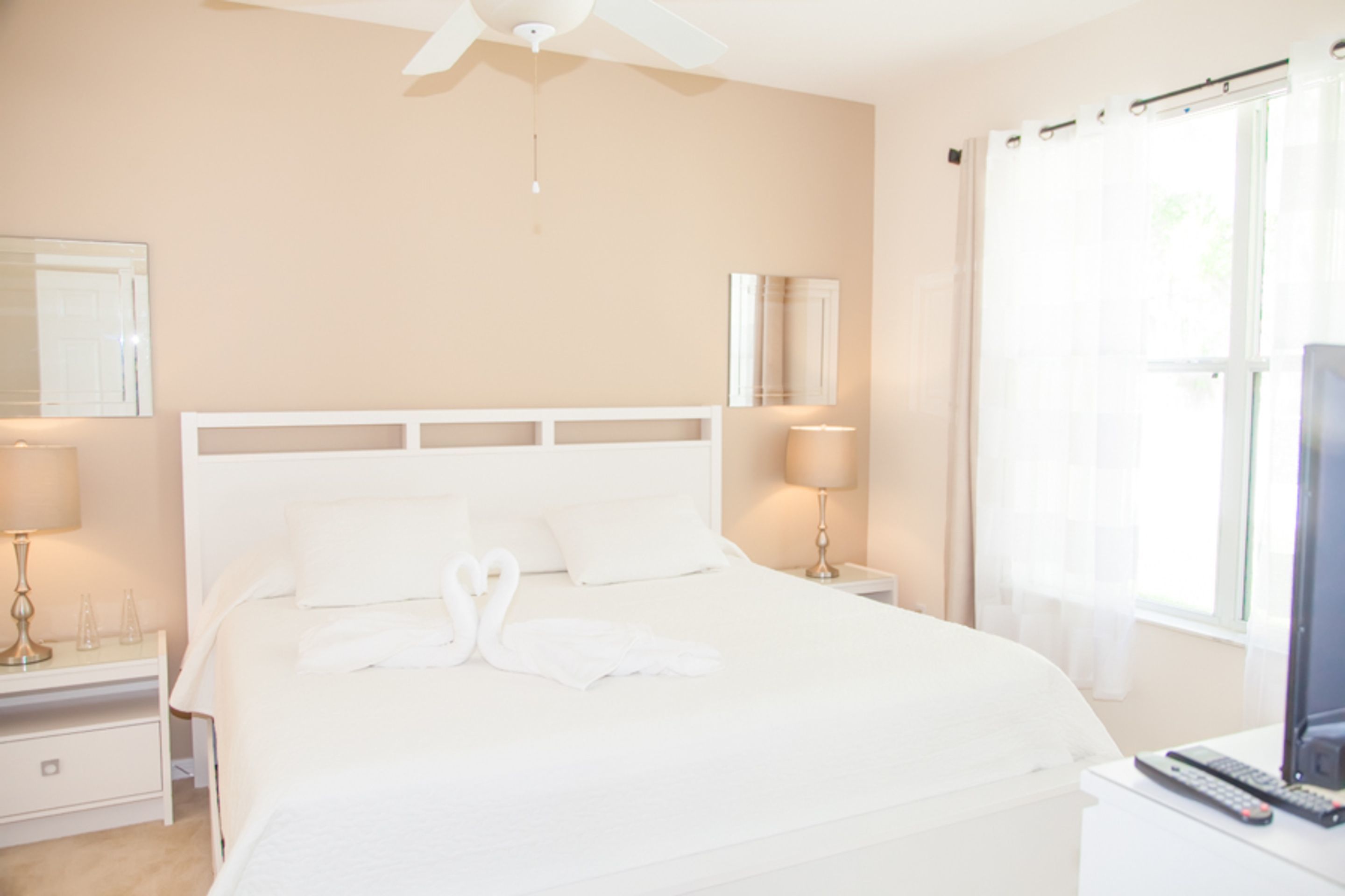 A hotel room with a large bed, a ceiling fan, bedside lamps, a TV, and a window with curtains.