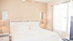 Une chambre d’hôtel avec un grand lit, un ventilateur de plafond, des lampes de chevet, une télévision et une fenêtre avec des rideaux.