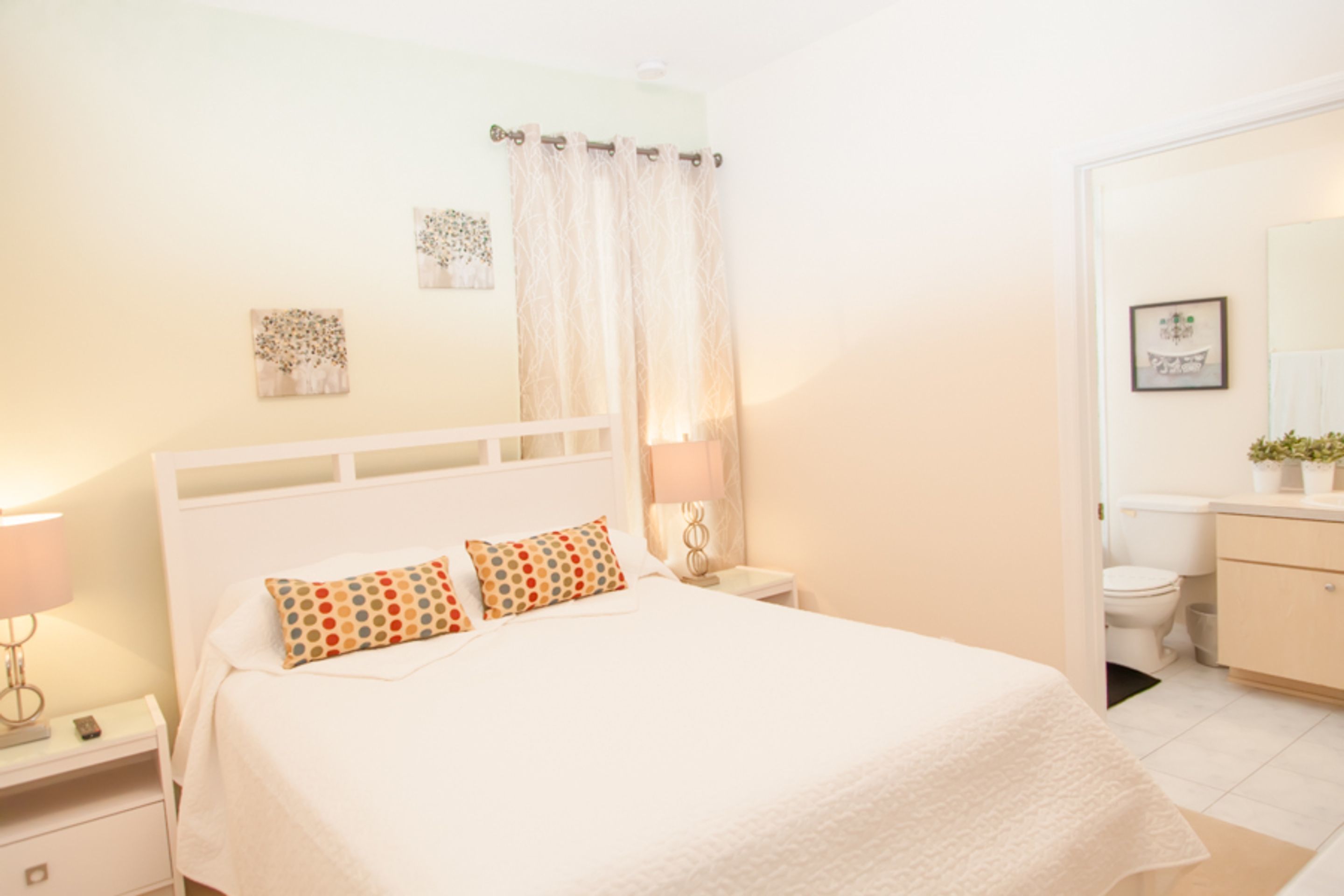 Un dormitorio con cama, mesita de noche y baño visible a través de una puerta abierta.