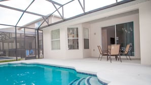 Une piscine dotée d’un toit en verre, un espace patio avec des chaises, et une porte-fenêtre coulissante donnant sur un espace extérieur abrité.