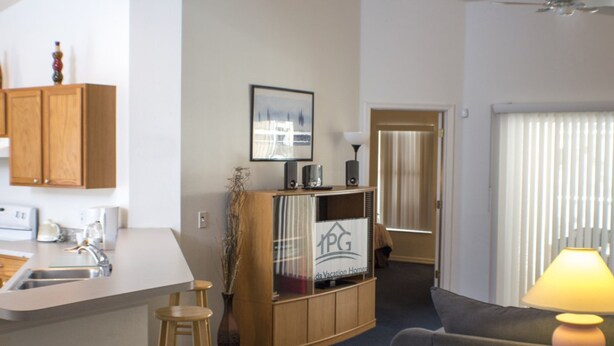 A compact living space with a kitchenette, a sofa, a lamp, and a cabinet with a sign. - Silver Creek 1217 (Clermont)