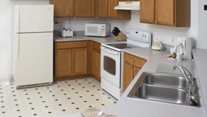 A kitchen with wooden cabinets, a white refrigerator, a microwave, an oven, a sink, and a tiled floor. - Silver Creek 1217 (Clermont)