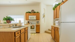 Una cocina con armarios de madera, un refrigerador blanco, un microondas, un horno y un fregadero.
